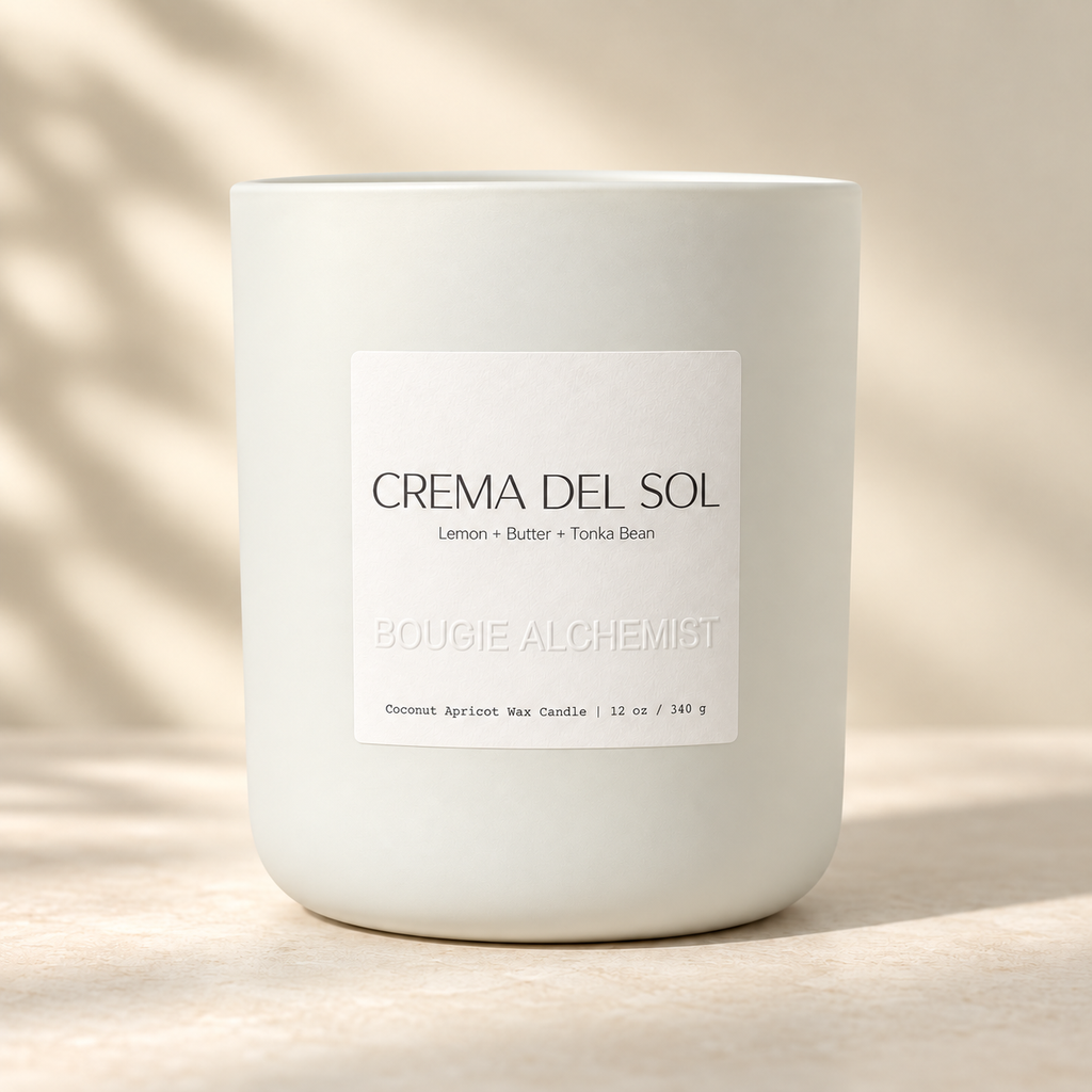 A white ceramic jar candle with a minimalist white label reading 'CREMA DEL SOL' and 'BOUGIE ALCHEMIST', set on a warm beige surface with soft leaf shadows.