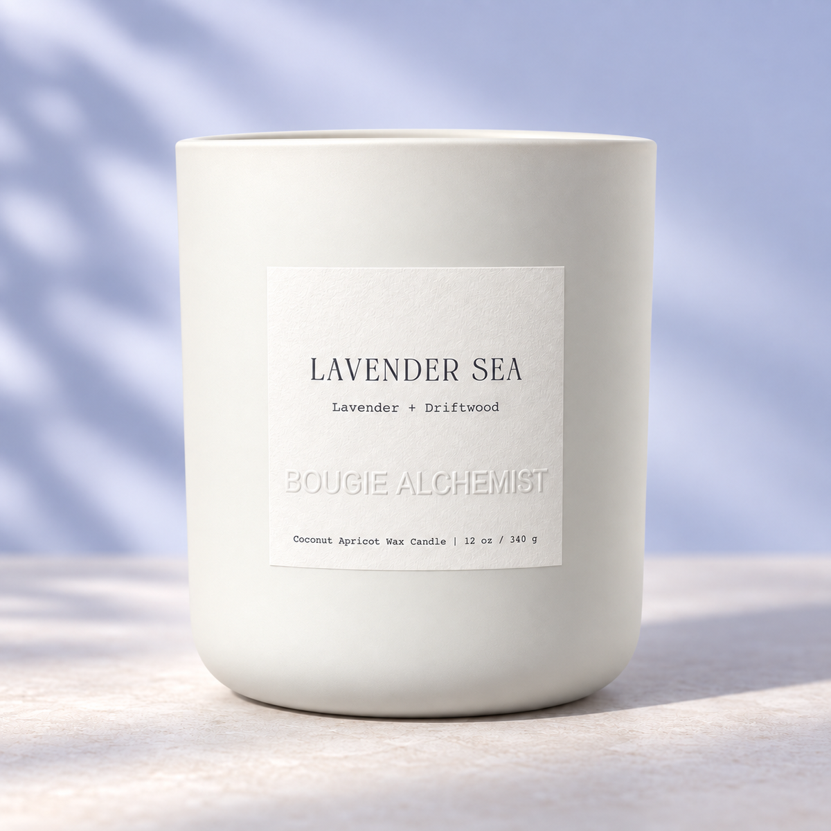 A matte white ceramic candle jar with a square white label reading 'LAVENDER SEA' and 'BOUGIE ALCHEMIST' on a light stone surface under soft natural light.