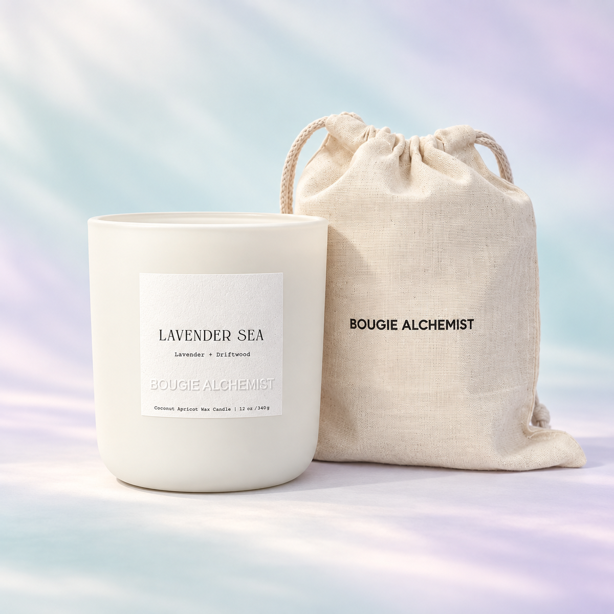 A white ceramic candle jar labeled 'LAVENDER SEA' stands next to a beige linen drawstring pouch printed with 'BOUGIE ALCHEMIST'. The background is a soft pastel gradient with light streaks.